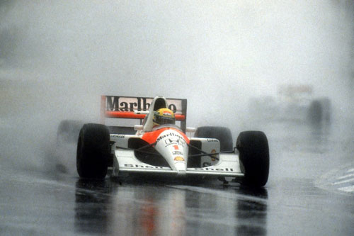 An old McLaren car driven by Ayrton Senna kicks up spray during a wet race